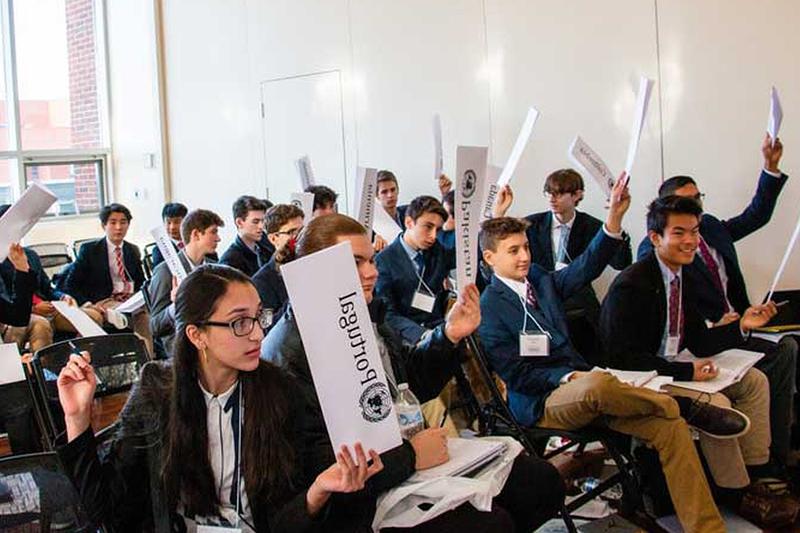 Students in a classroom all raising their hands.